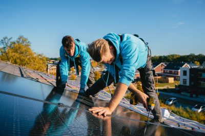 Twee zonnepanelenmonteurs op het dak aan het werk in de zon